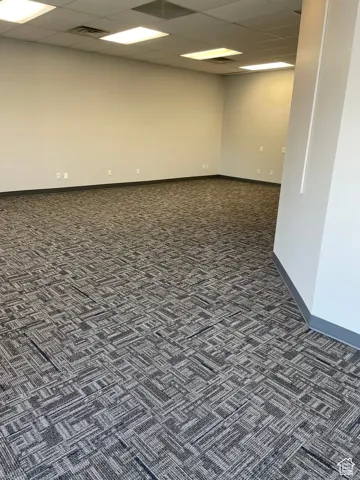 Empty room with a drop ceiling and dark colored carpet