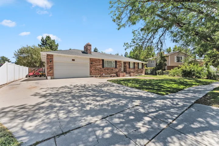 View of front of property with brick siding, driveway, a garage, and a chimney