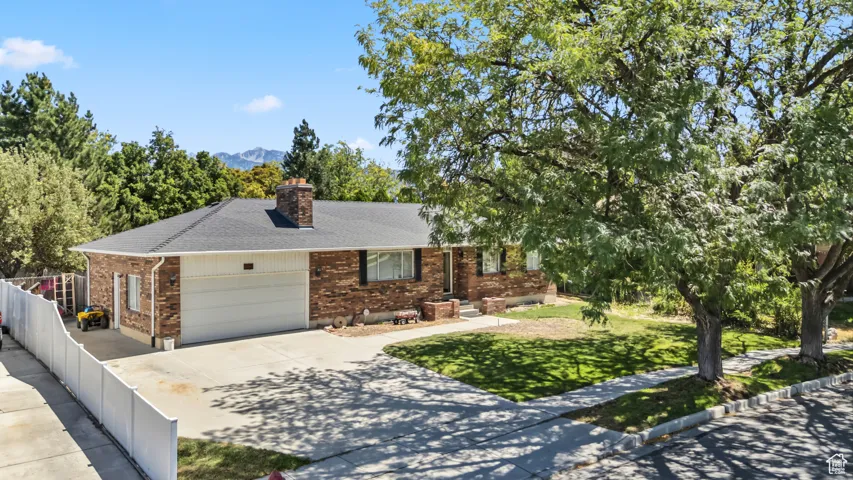 Ranch-style home featuring brick siding, driveway, a chimney, an attached garage, and roof with shingles