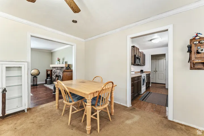 Dining space with crown molding, light colored carpet, a stone fireplace, and a ceiling fan