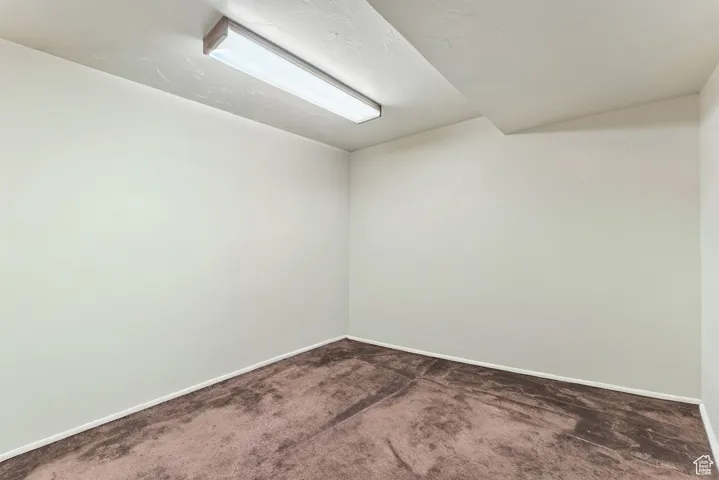 Unfurnished room with dark carpet and vaulted ceiling