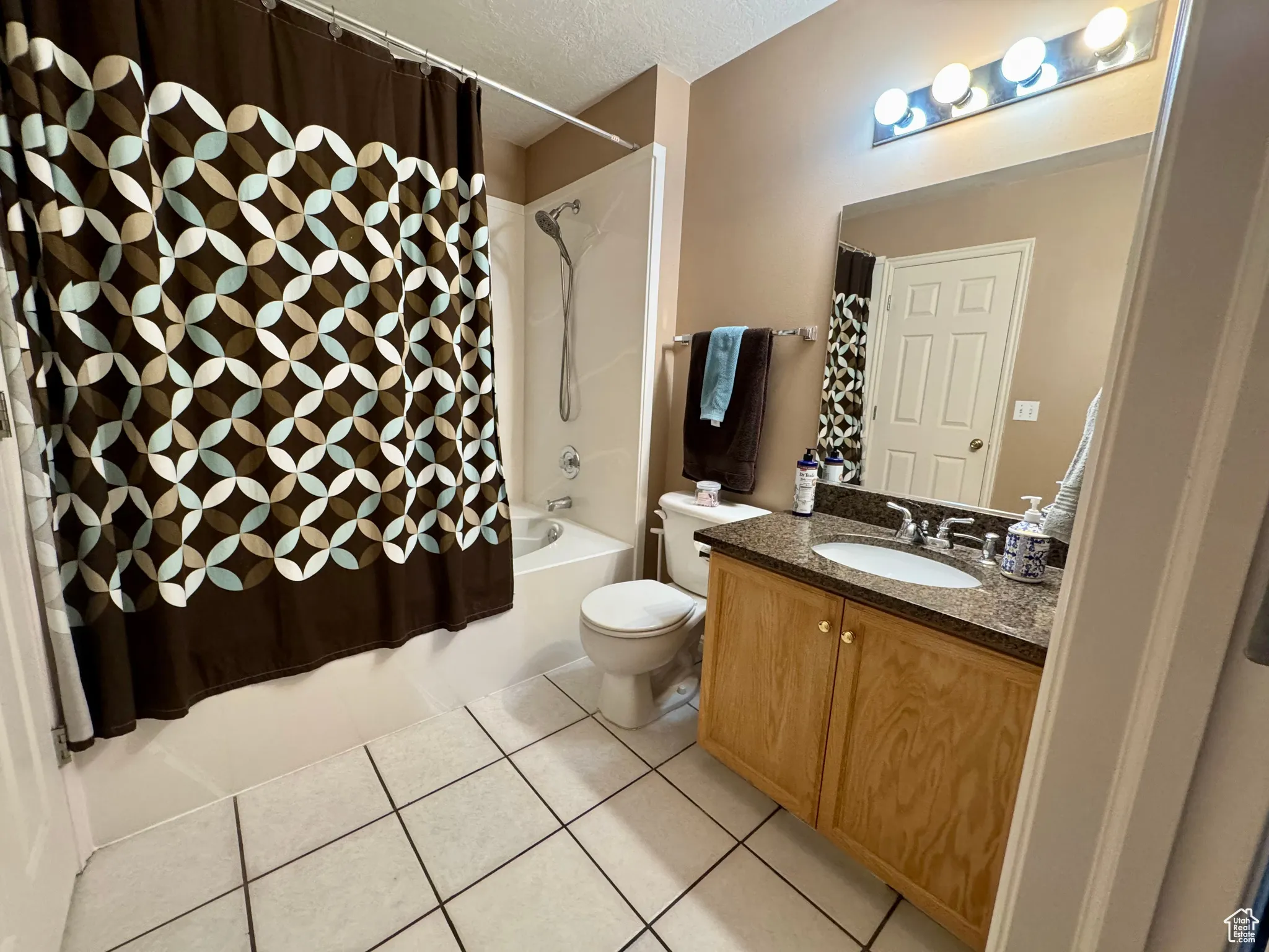 Full bathroom featuring light tile patterned flooring, shower / bath combination with curtain, a textured ceiling, and vanity