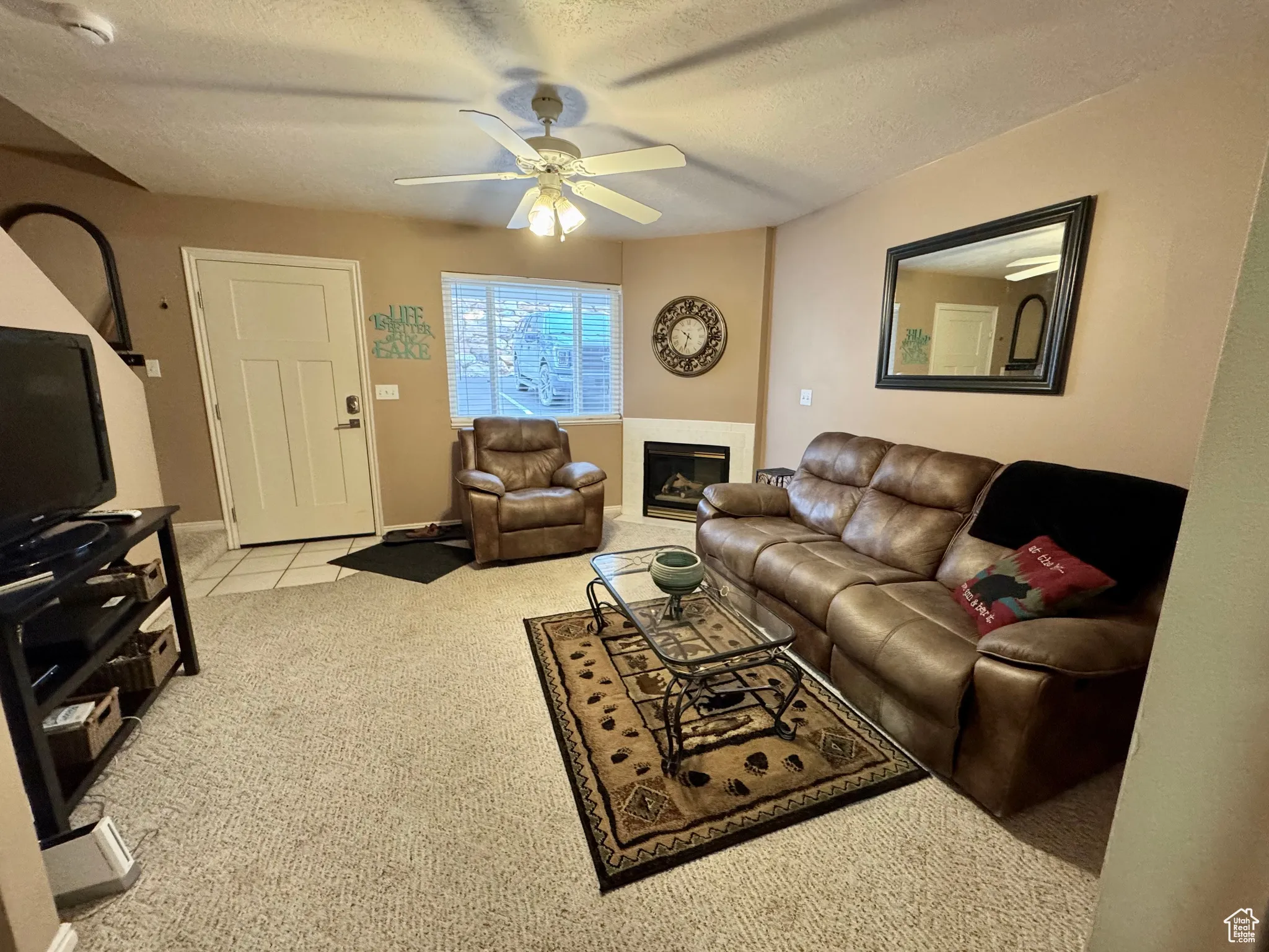 Living area featuring a textured ceiling, light colored carpet, a glass covered fireplace, a ceiling fan, and light tile patterned floors