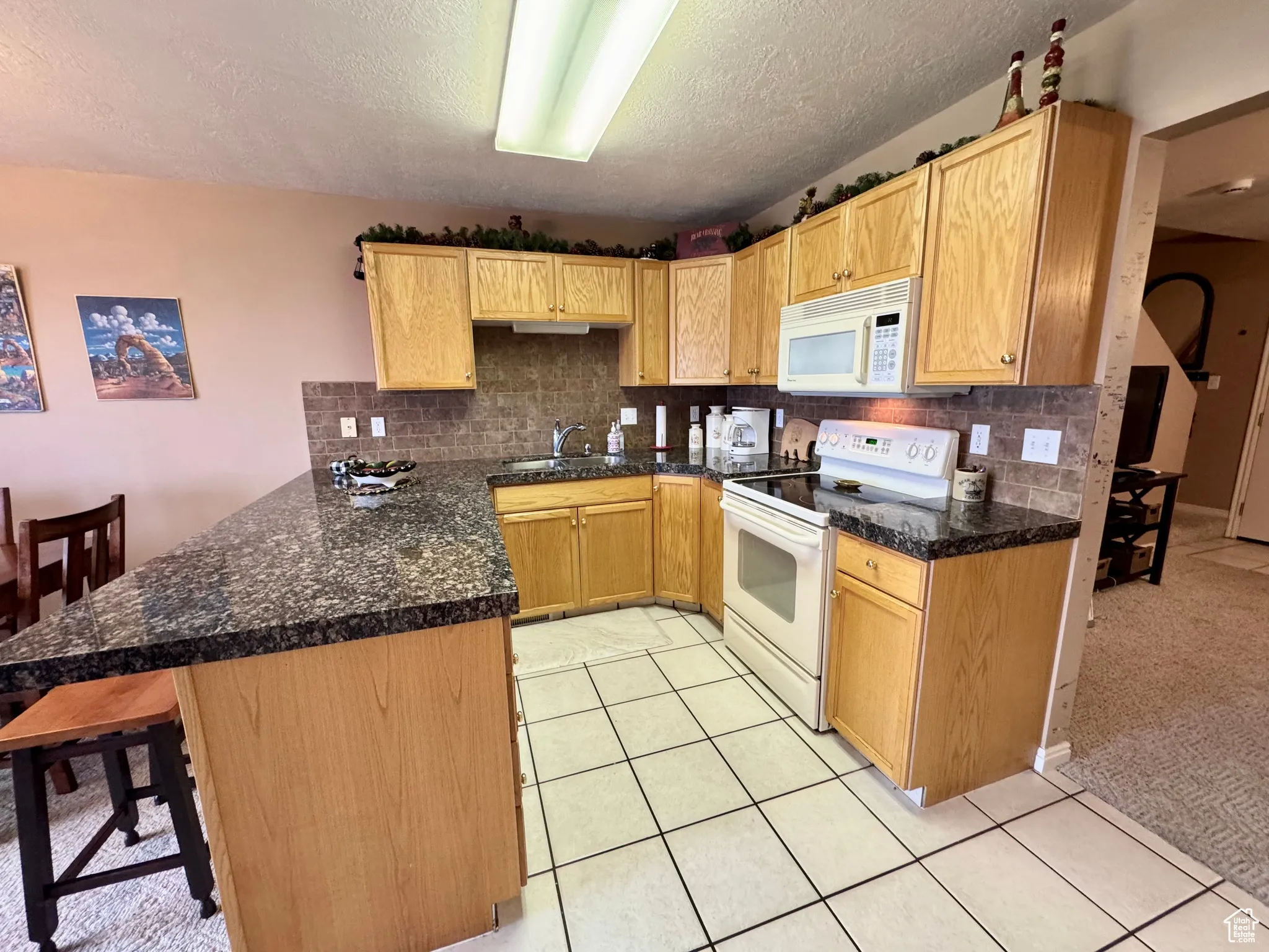 Kitchen featuring backsplash, white appliances, a peninsula, a breakfast bar area, and a textured ceiling