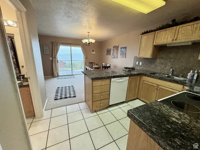 Kitchen with a peninsula, light tile patterned floors, decorative backsplash, a chandelier, and a textured ceiling