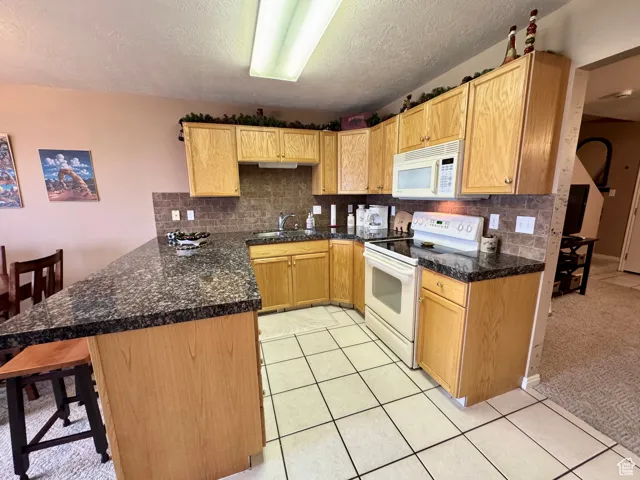 Kitchen featuring backsplash, white appliances, a peninsula, a breakfast bar area, and a textured ceiling