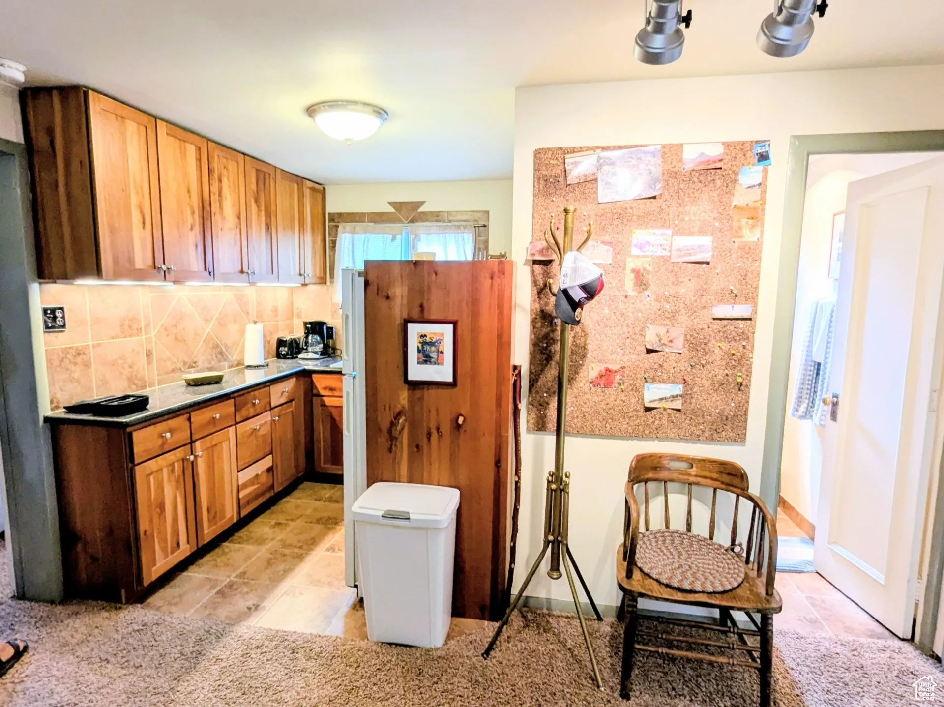 Kitchen with light tile patterned floors, brown cabinets, backsplash, light carpet, and rail lighting