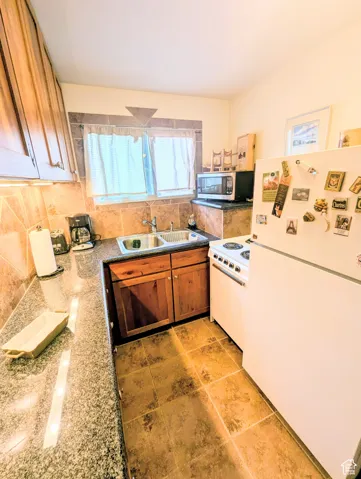 Kitchen featuring white appliances, tasteful backsplash, dark stone countertops, brown cabinets, and light tile patterned flooring
