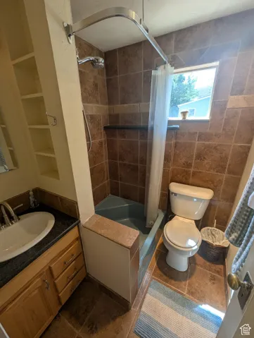 Full bath with shower / bath combo with shower curtain, vanity, dark tile patterned flooring, and tile walls