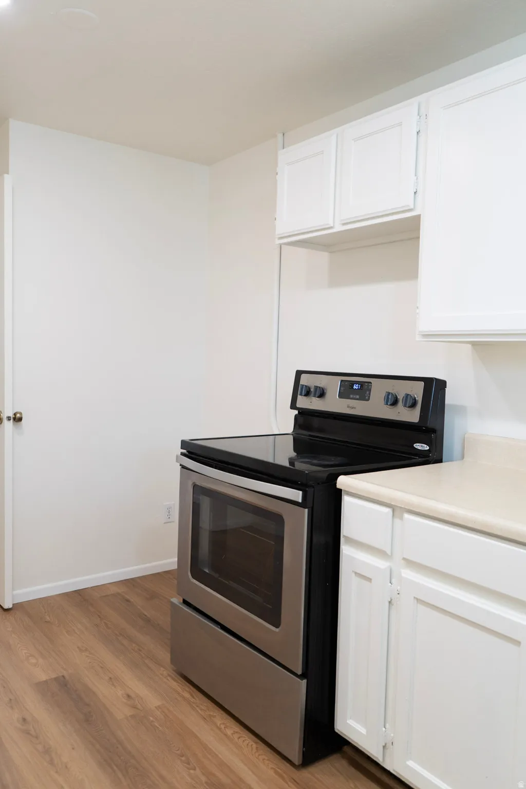 Kitchen with electric range, light countertops, white cabinetry, and light wood finished floors