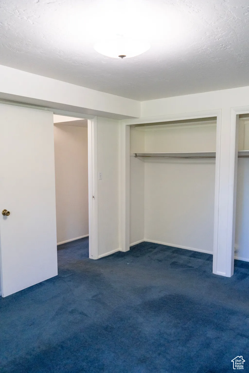 Unfurnished bedroom featuring a textured ceiling, dark colored carpet, and multiple closets