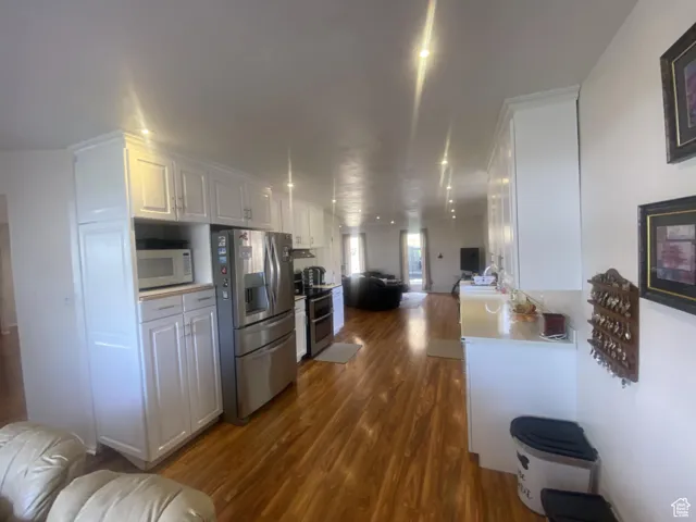 Kitchen with open floor plan, white cabinetry, appliances with stainless steel finishes, and dark wood-style floors