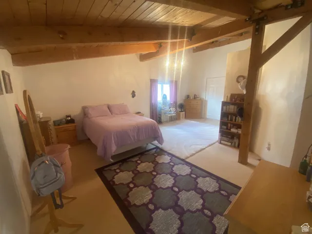 Bedroom with a wood ceiling with exposed beams and carpet