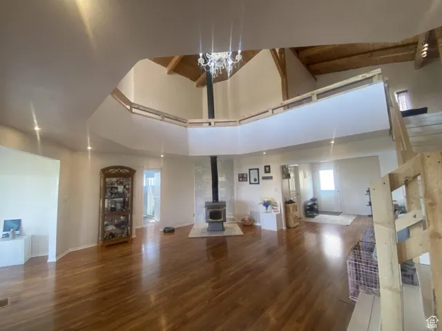 Living room with beam ceiling, wood finished floors, a wood stove, a towering ceiling, and stairs