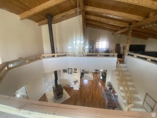 Unfurnished living room with wood finished floors, a wood ceiling with exposed beams, a wood stove, and high vaulted ceiling