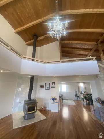 Living room featuring a wood stove, a wood ceiling with exposed beams, dark wood finished floors, high vaulted ceiling, and a chandelier