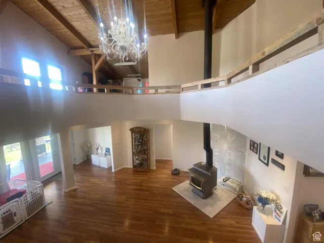 Unfurnished living room featuring high vaulted ceiling, a wood stove, dark wood-type flooring, healthy amount of natural light, and a wood ceiling with exposed beams