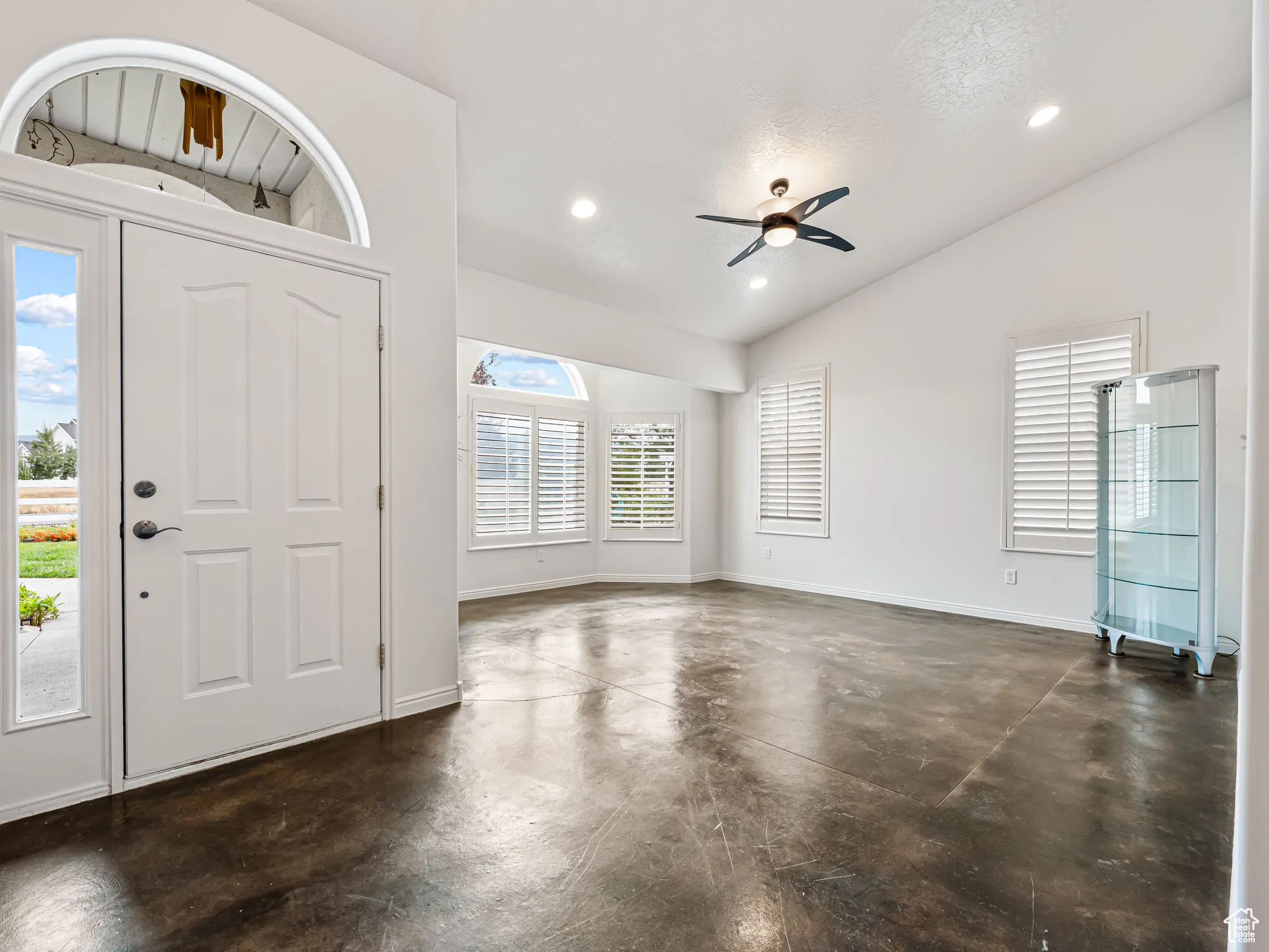 Foyer entrance to living room with finished concrete floors, plenty of natural light, ceiling fan, recessed lighting, and high vaulted ceiling
