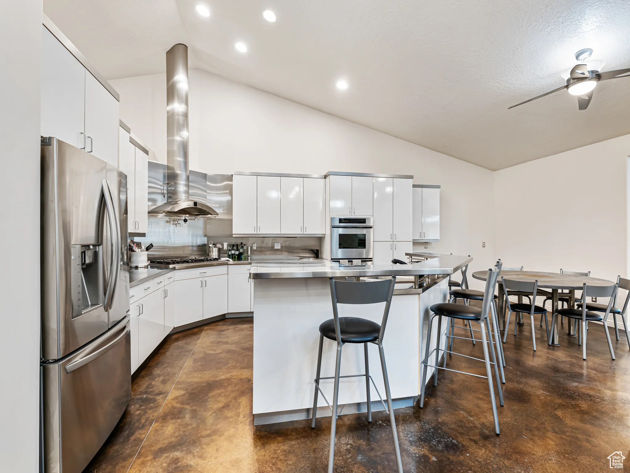 True Chef's Kitchen featuring white cabinetry, appliances with stainless steel finishes, a breakfast bar area, a ceiling fan, and a center island