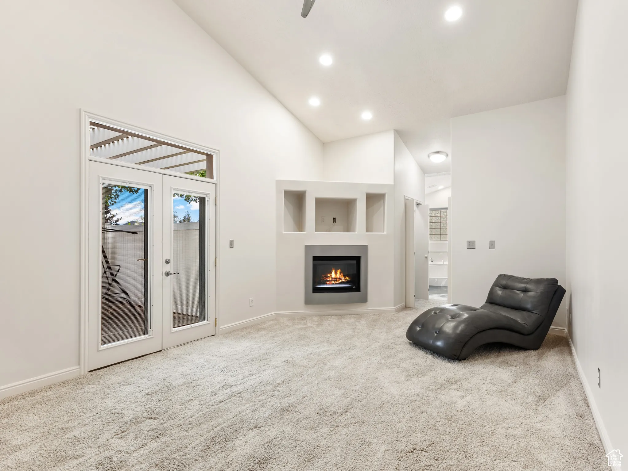 Unfurnished room with high vaulted ceiling, light colored carpet, recessed lighting, a warm lit fireplace, and french doors
