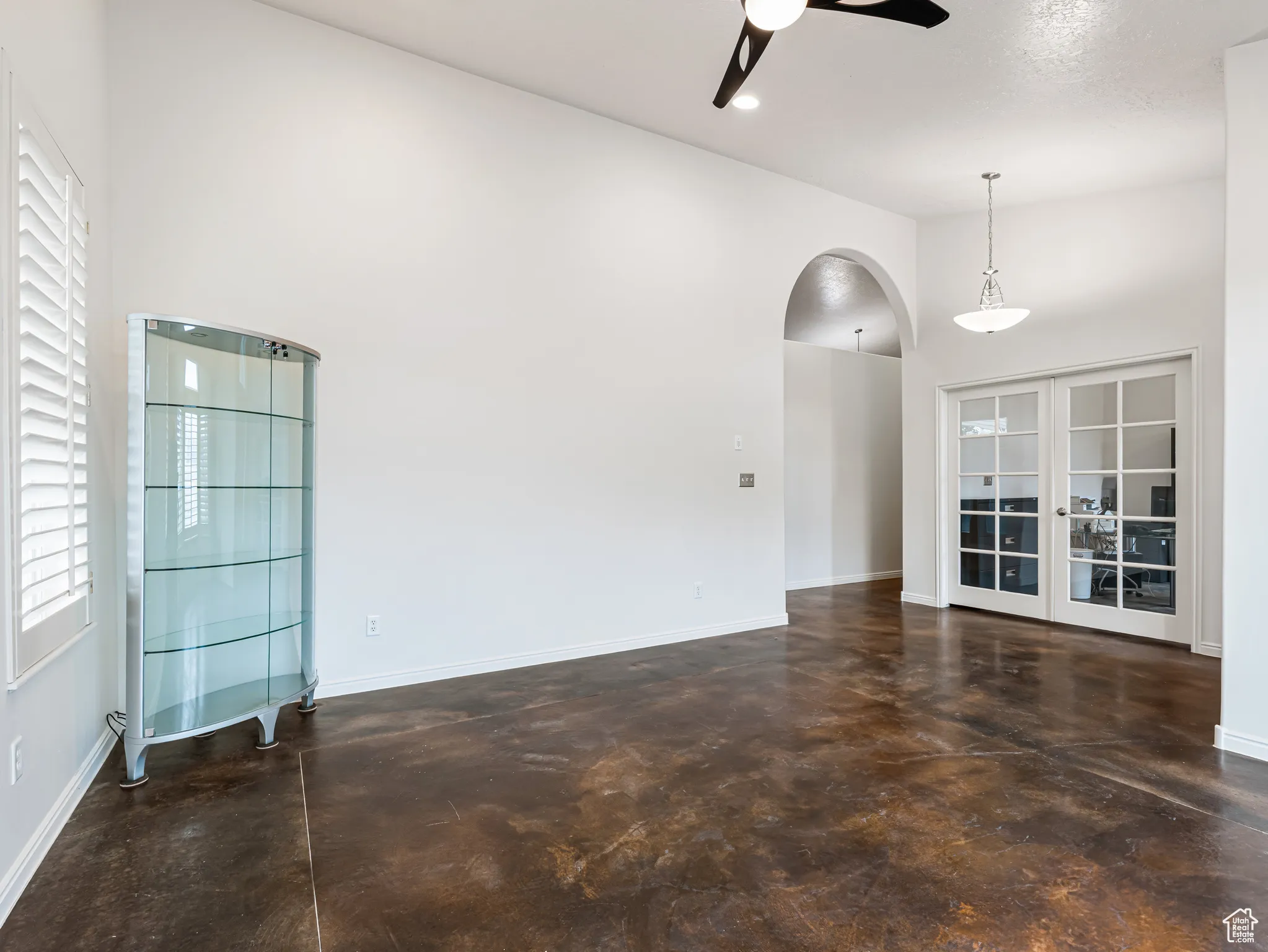 living room featuring finished concrete floors,  tall vaulted ceiling, and french doors to a flex room/ Office. Archways throughout the home.