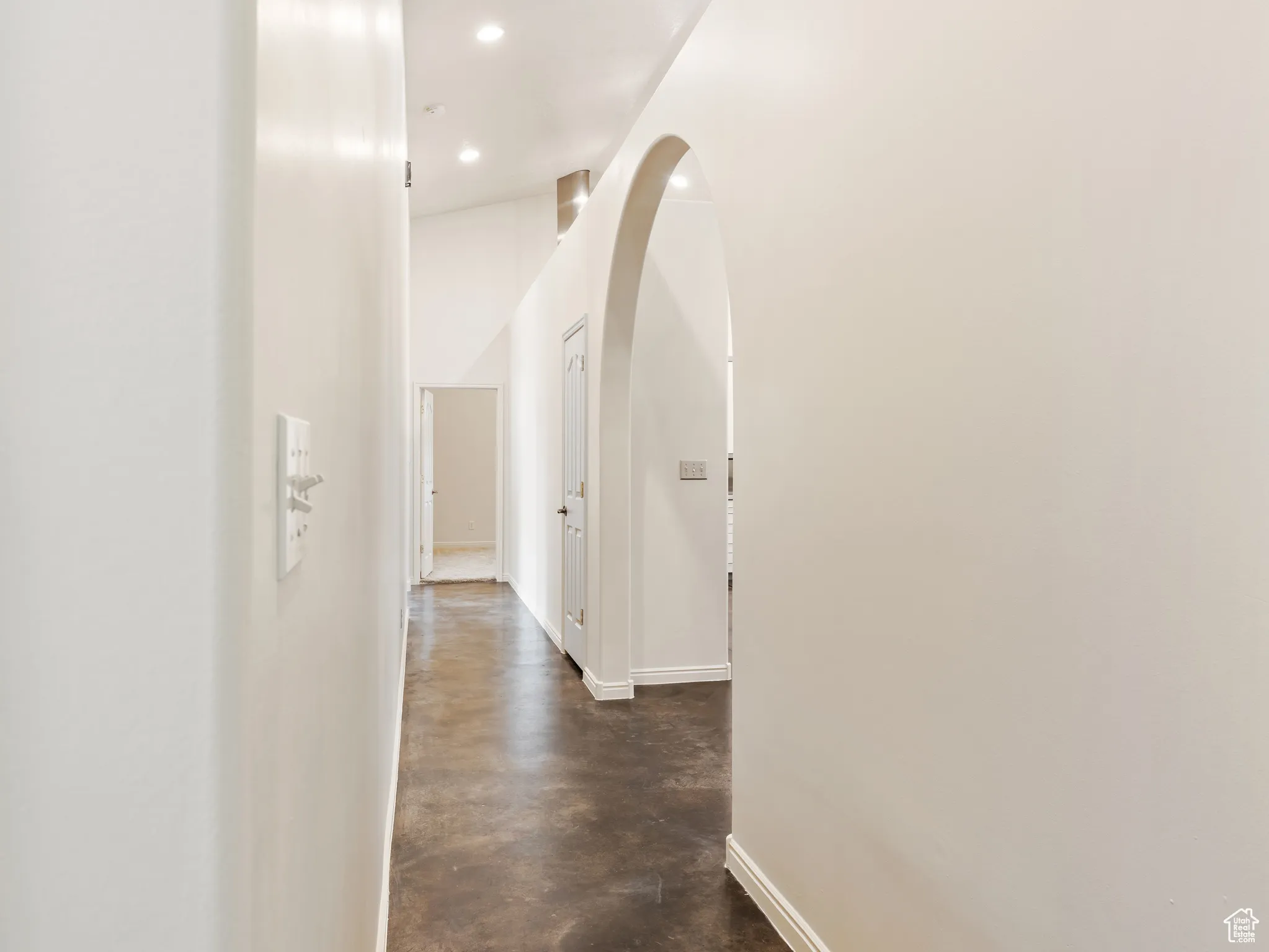 Hallway with finished concrete flooring, arched walkways, and recessed lighting