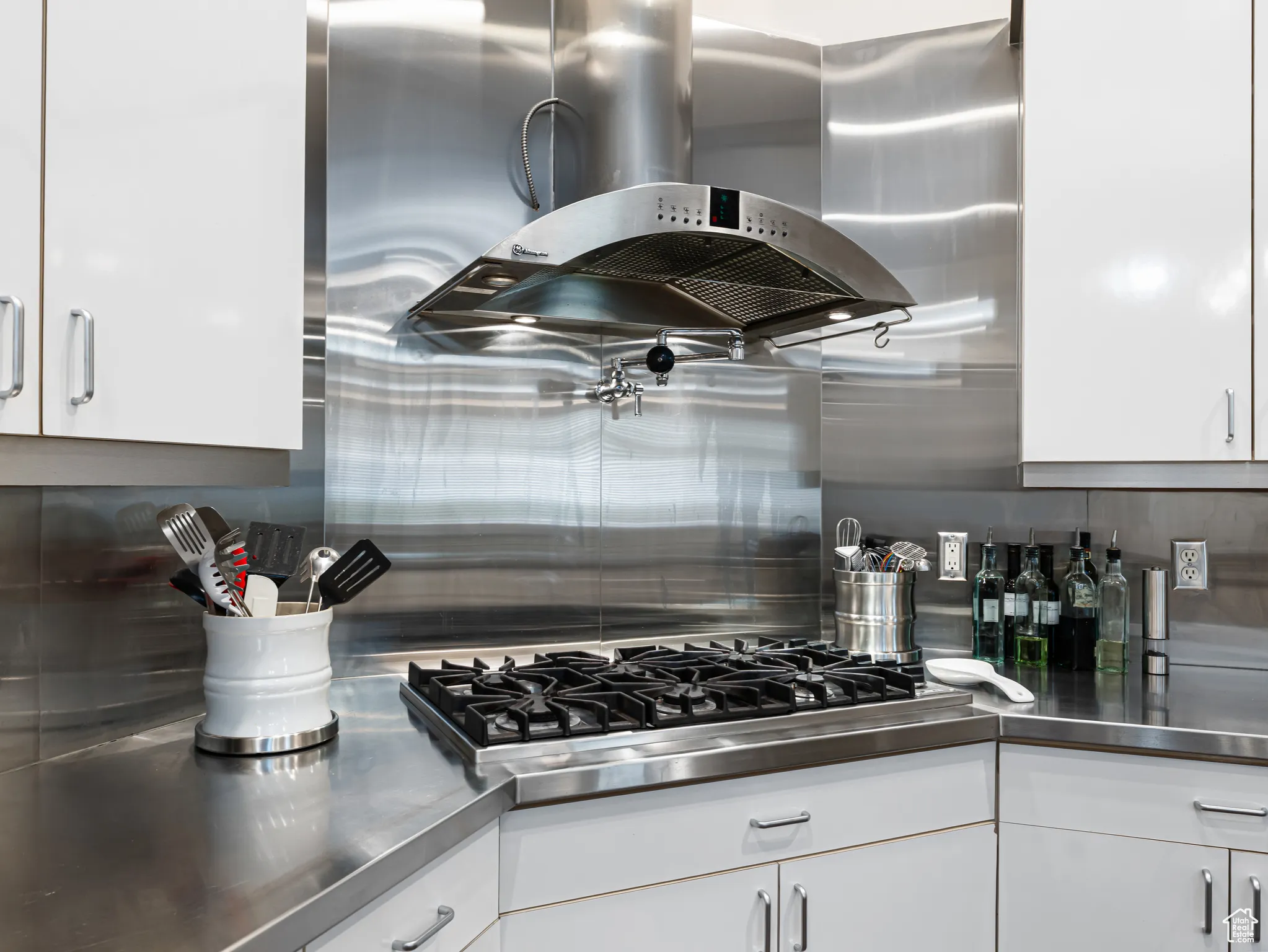 Kitchen featuring stainless steel countertops, island range hood, white cabinets, and stainless steel gas cooktop