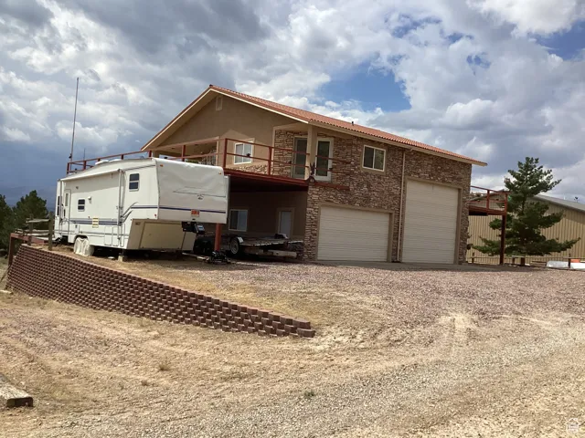 Rear view of house with driveway, stone siding, a deck, a garage, and a balcony