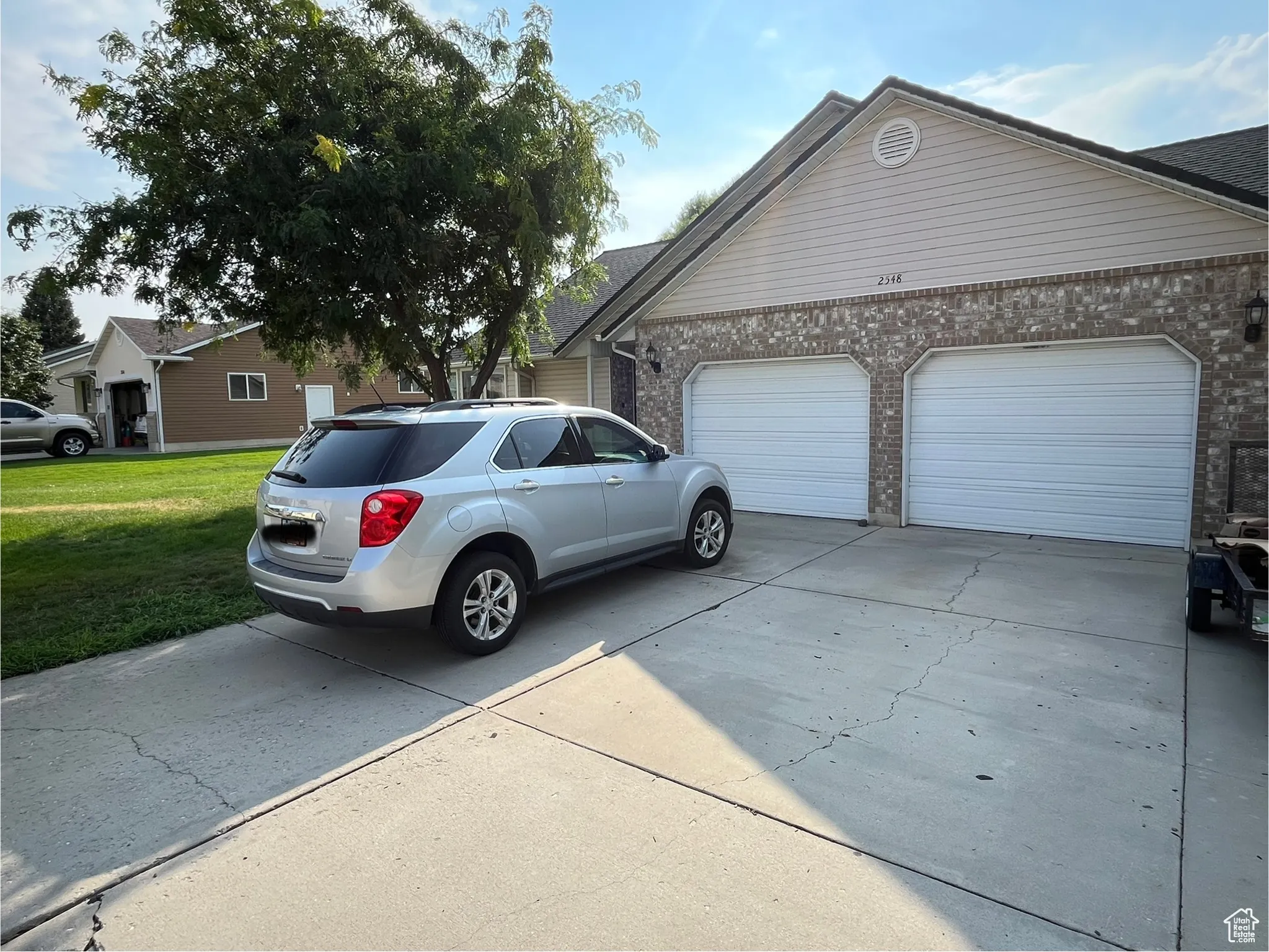 View of side of home with concrete driveway, brick siding, a garage, and a lawn