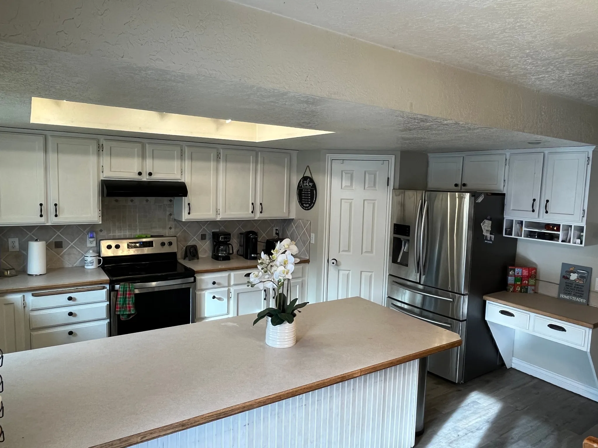 Kitchen featuring light countertops, appliances with stainless steel finishes, white cabinets, a textured ceiling, and under cabinet range hood