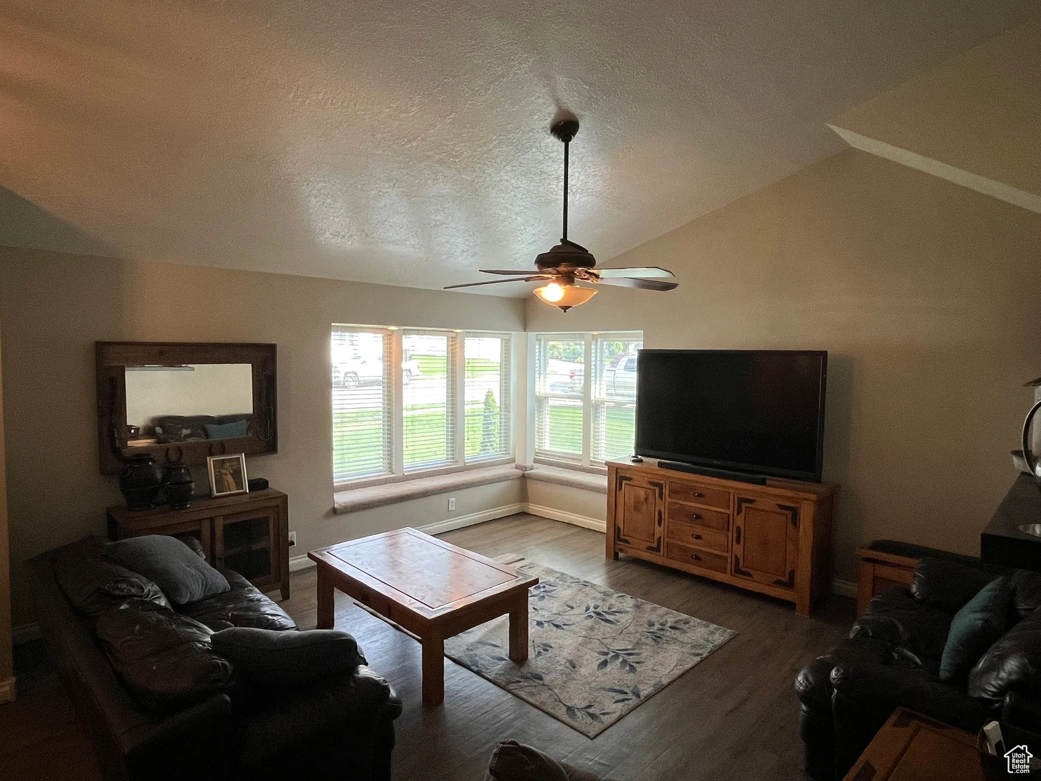 Living room with vaulted ceiling, wood finished floors, a textured ceiling, and a ceiling fan