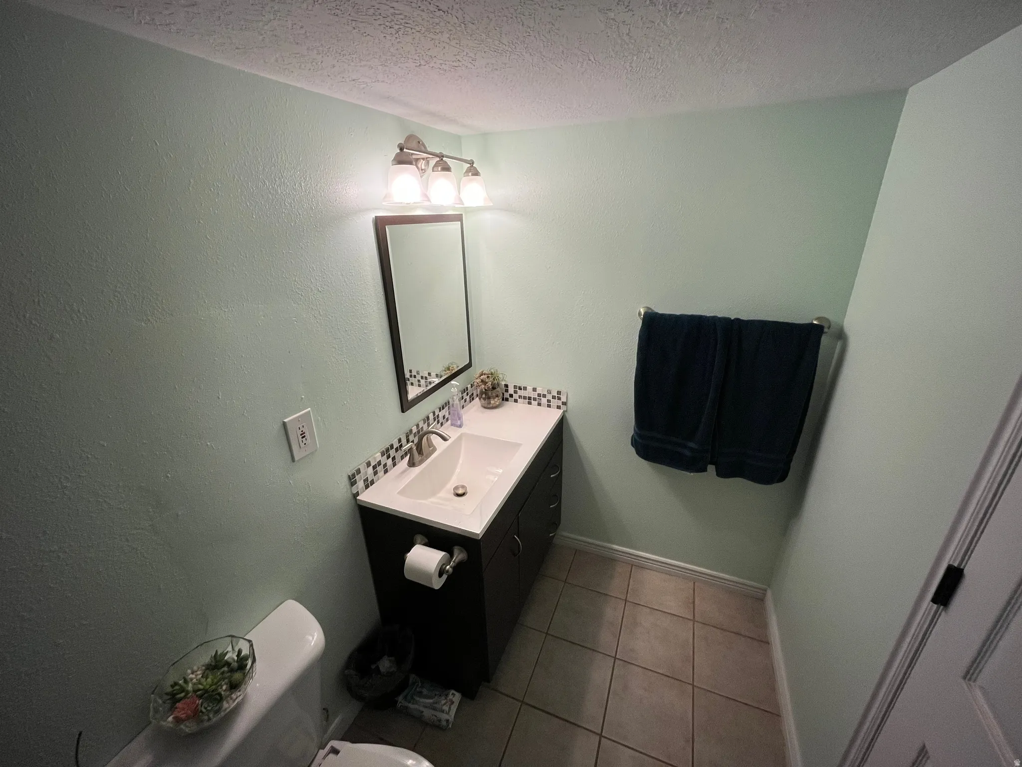 Half bathroom with vanity, a textured ceiling, tile patterned flooring, and a textured wall