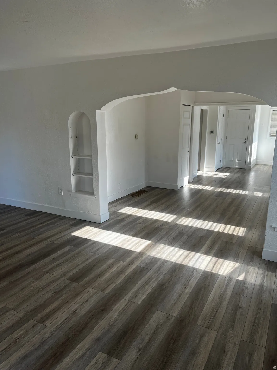 Spare room featuring arched walkways, dark wood-type flooring, and built in shelves