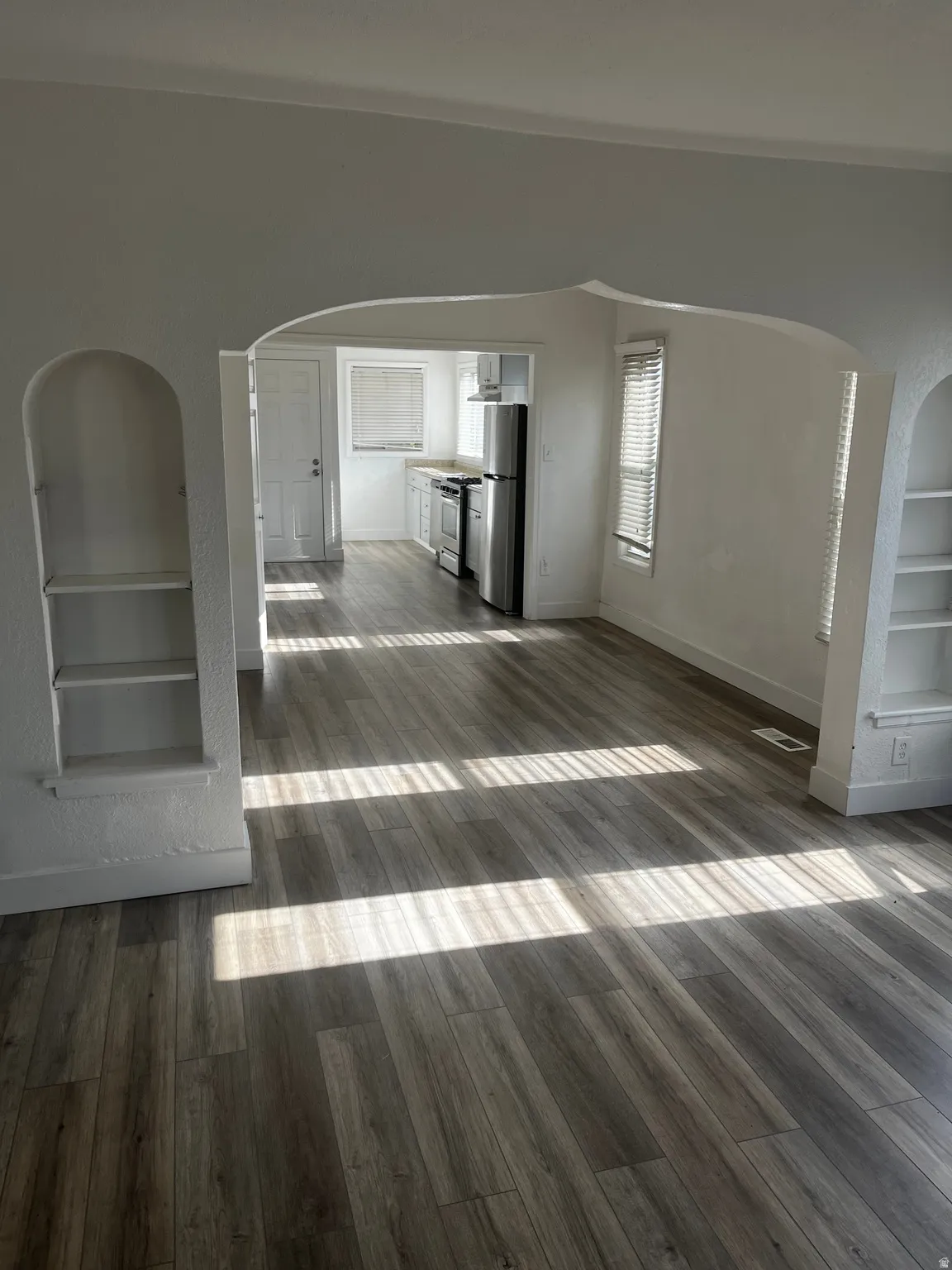 Unfurnished living room featuring arched walkways, built in shelves, and dark wood-style floors