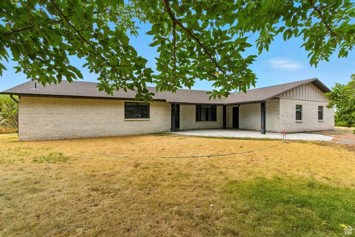 Back of property featuring brick siding, a patio, a yard, roof with shingles, and board and batten siding
