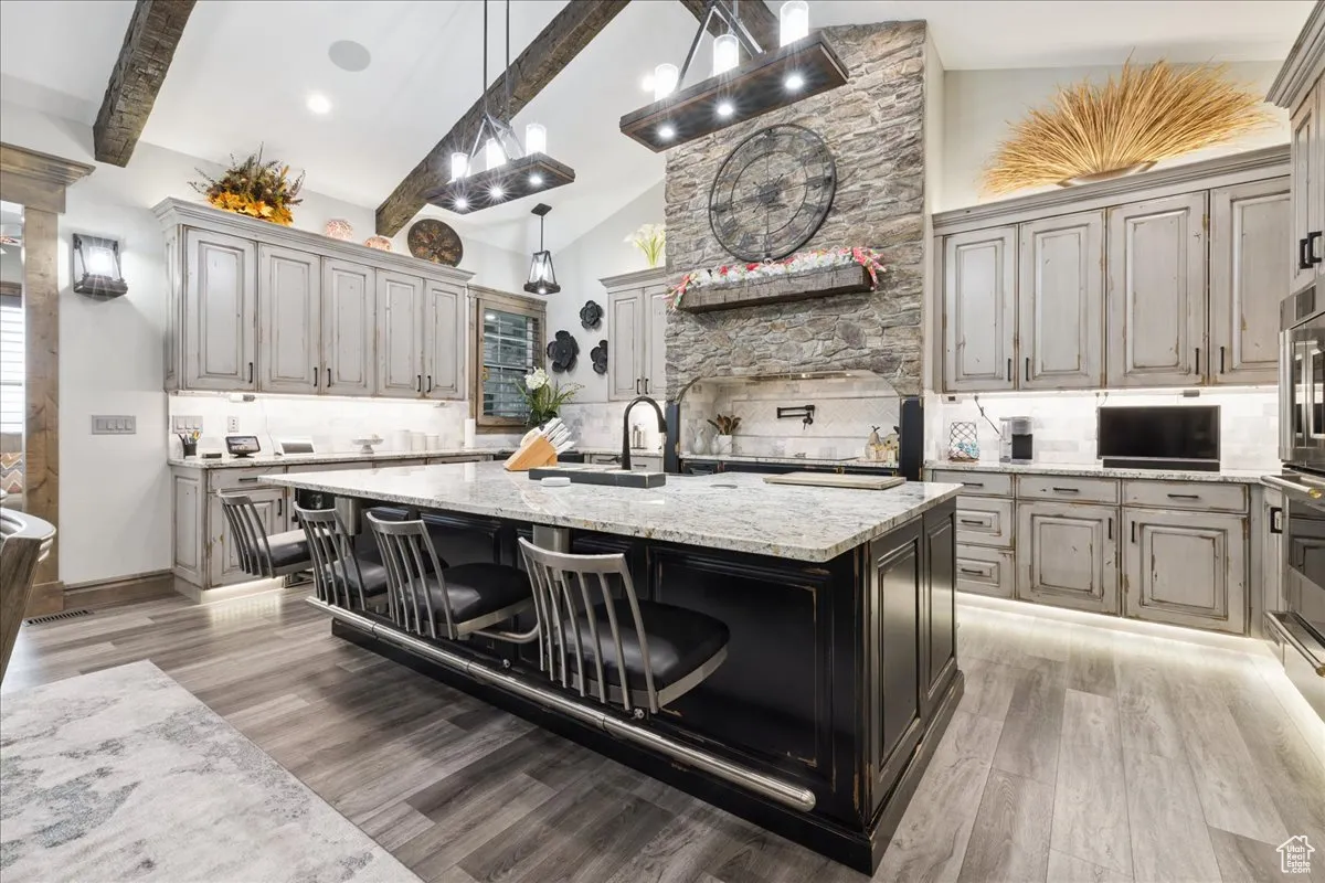 Kitchen featuring tasteful backsplash, light stone countertops, a breakfast bar area, beam ceiling, and pendant lighting