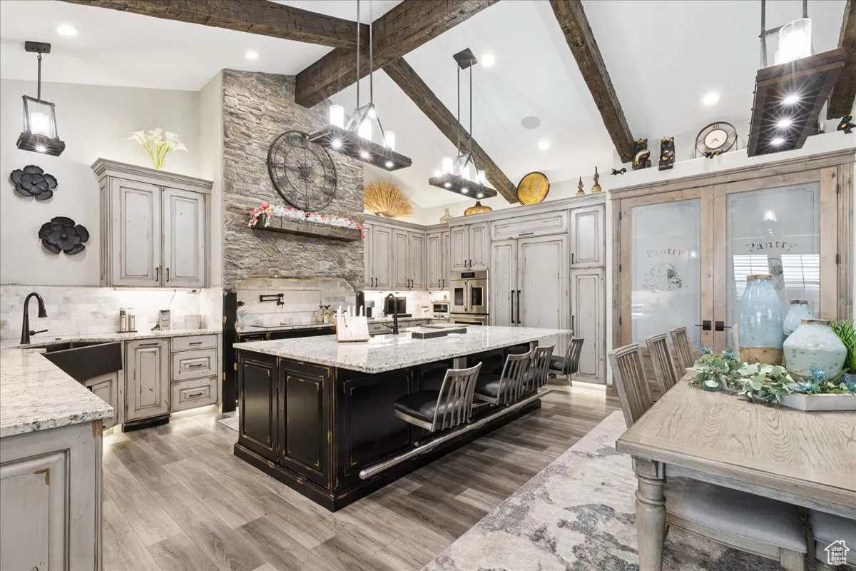 Kitchen with light stone countertops, pendant lighting, decorative backsplash, high vaulted ceiling, and an island with sink