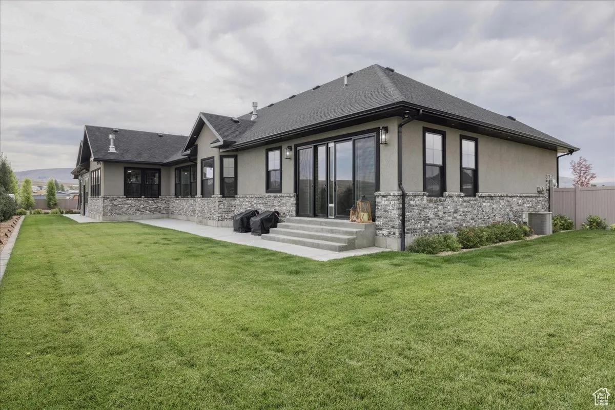 Rear view of property featuring stone siding, a patio area, roof with shingles, and stucco siding