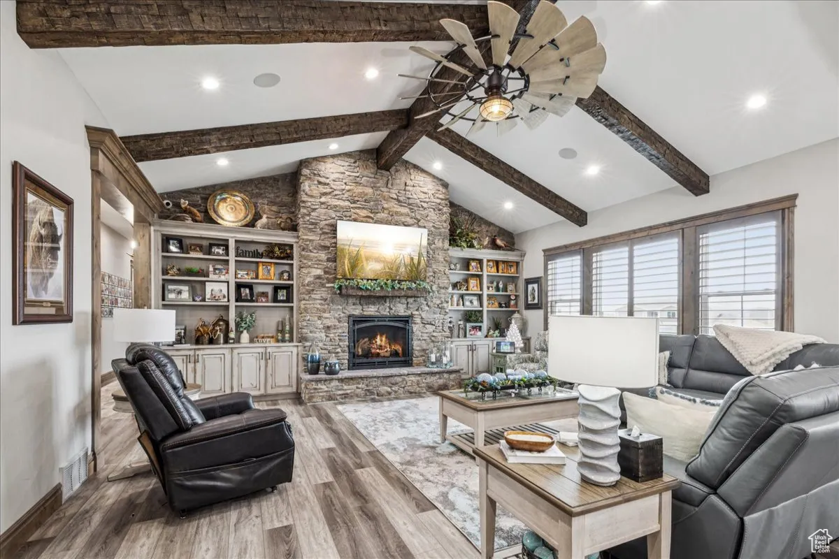 Living area featuring a fireplace, beam ceiling, wood finished floors, a ceiling fan, and high vaulted ceiling