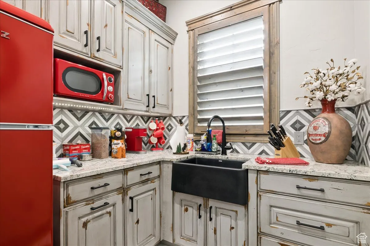 Kitchen featuring freestanding refrigerator, decorative backsplash, and light stone counters