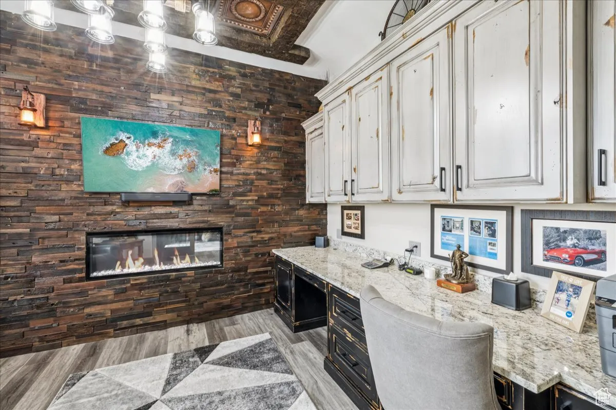 Bar area featuring a glass covered fireplace, light stone countertops, light wood-style flooring, and dark cabinetry