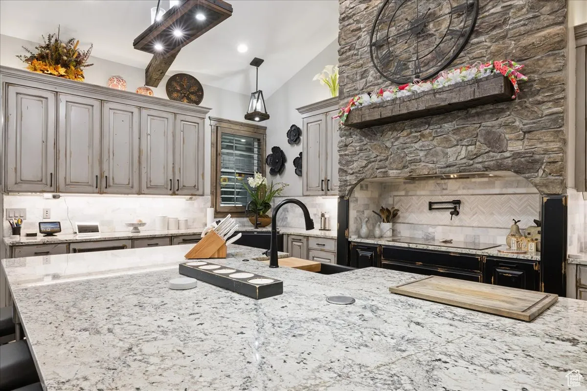 Kitchen with backsplash, vaulted ceiling, light stone counters, hanging light fixtures, and gray cabinetry