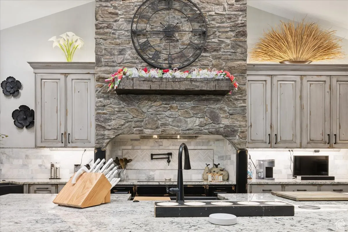 Kitchen featuring backsplash, light stone counters, and lofted ceiling