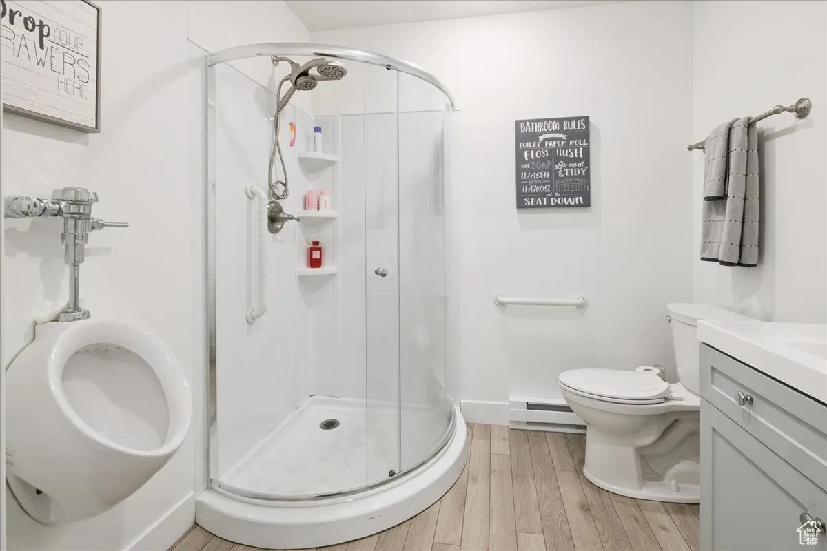 Full bathroom featuring vanity, a shower stall, light wood finished floors, and a baseboard heating unit