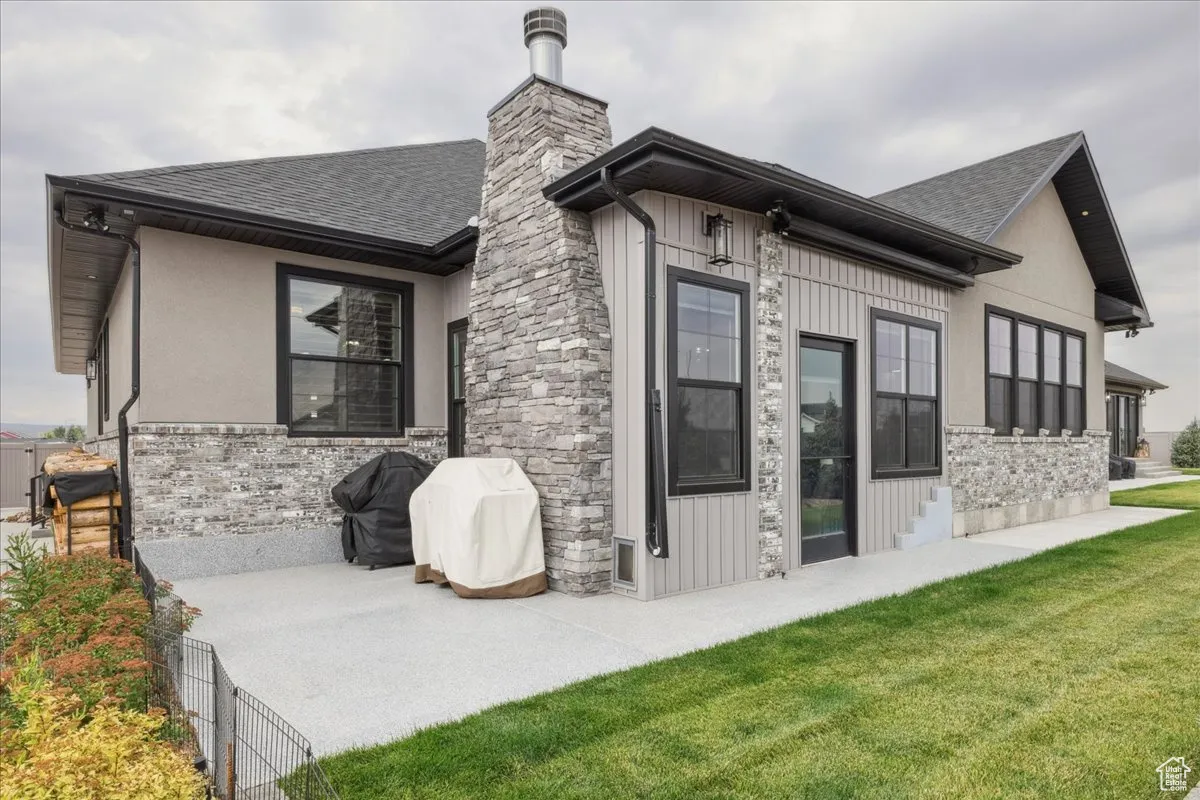 Rear view of property with a lawn, roof with shingles, stone siding, a chimney, and board and batten siding