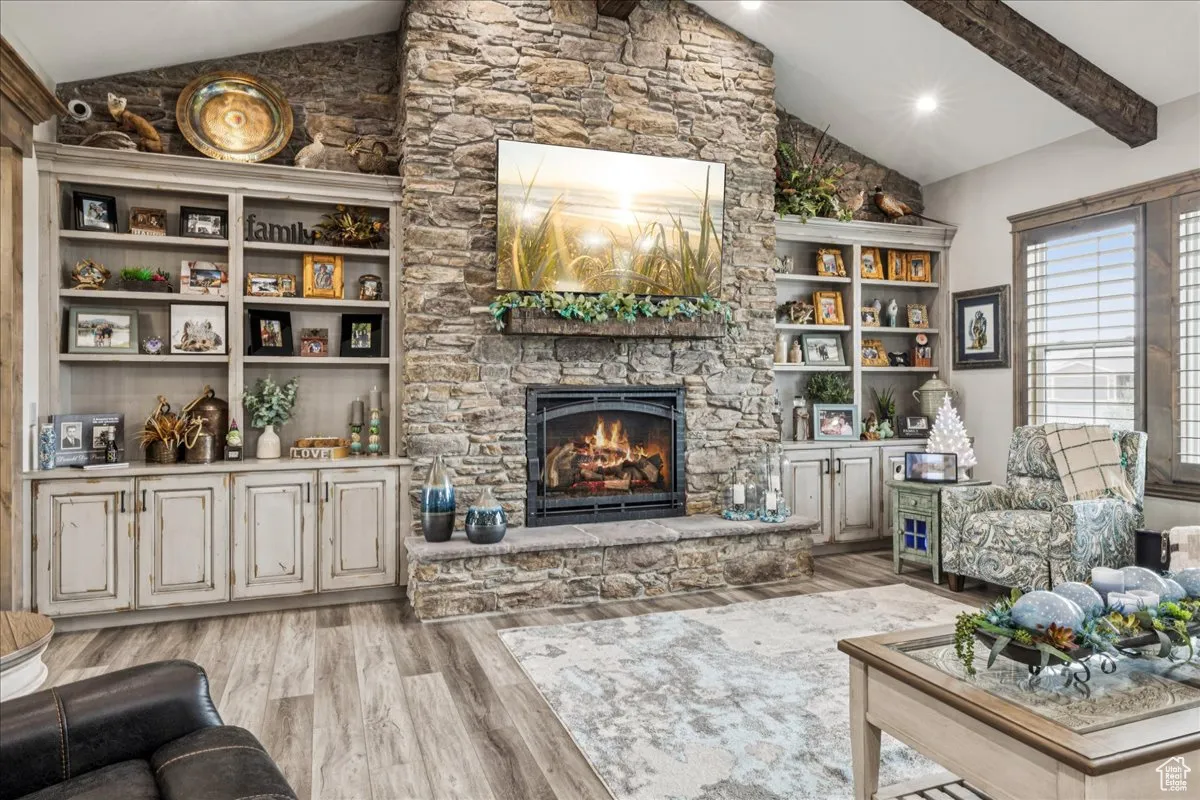 Living room featuring light wood-style floors, beam ceiling, a fireplace, built in features, and high vaulted ceiling