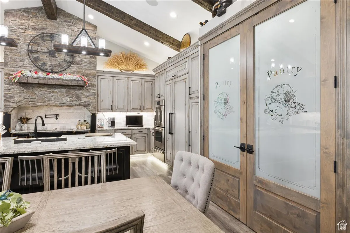 Kitchen featuring beam ceiling, light stone countertops, tasteful backsplash, pendant lighting, and a chandelier