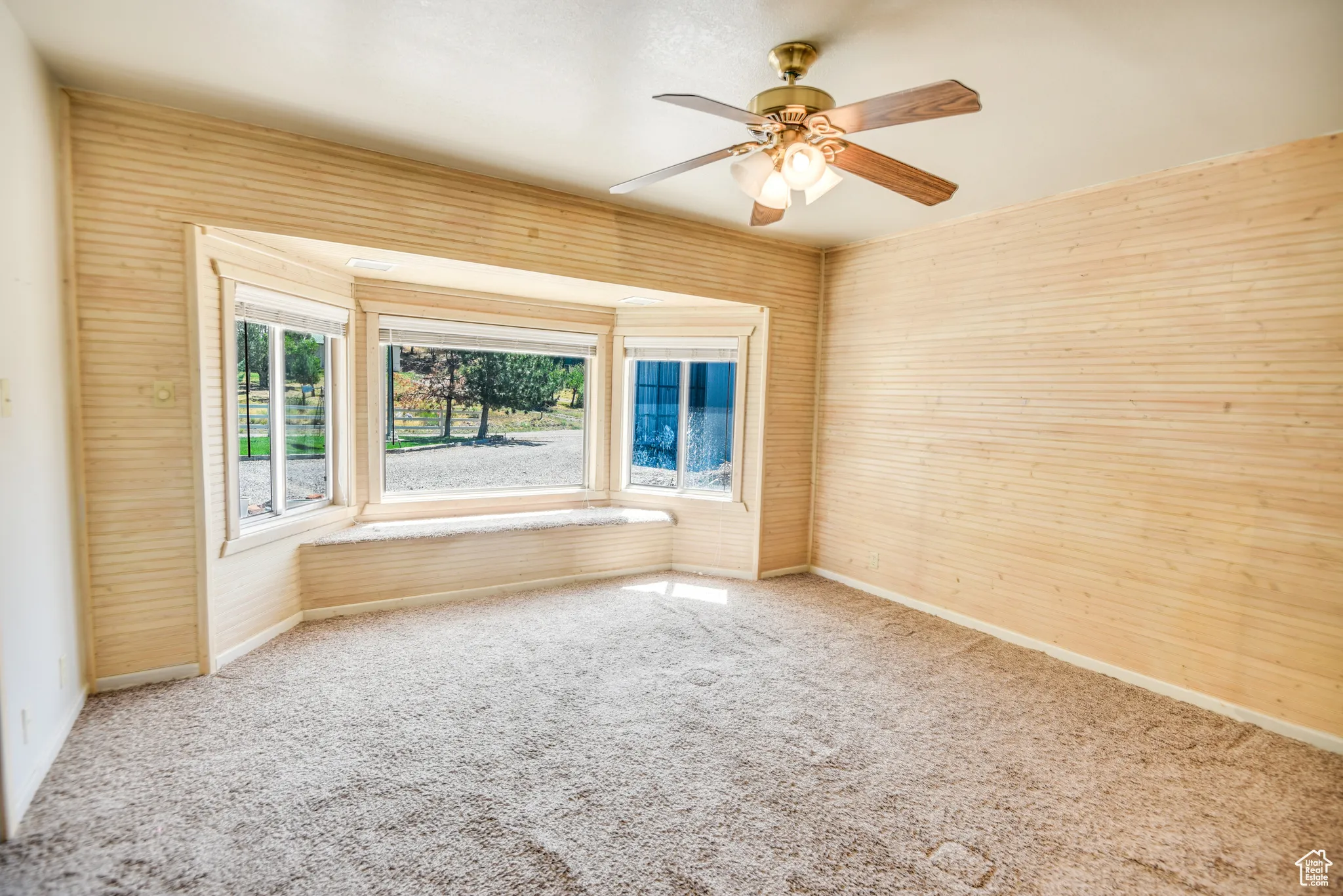 Carpeted spare room with a ceiling fan and wood walls