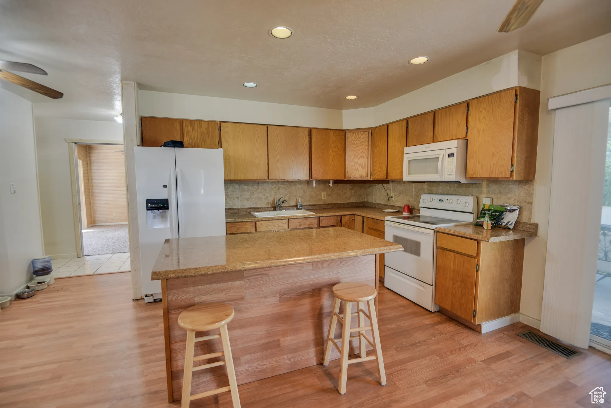 Kitchen with a ceiling fan, white appliances, backsplash, a kitchen breakfast bar, and recessed lighting