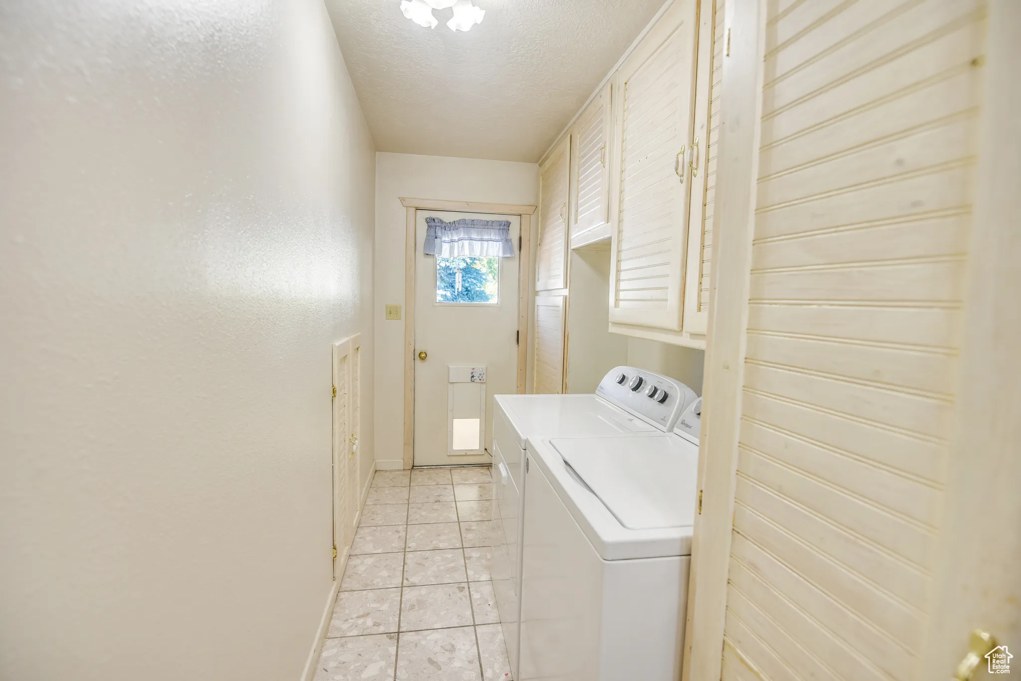 Laundry room with cabinet space, a textured ceiling, washer and clothes dryer, and light tile patterned floors